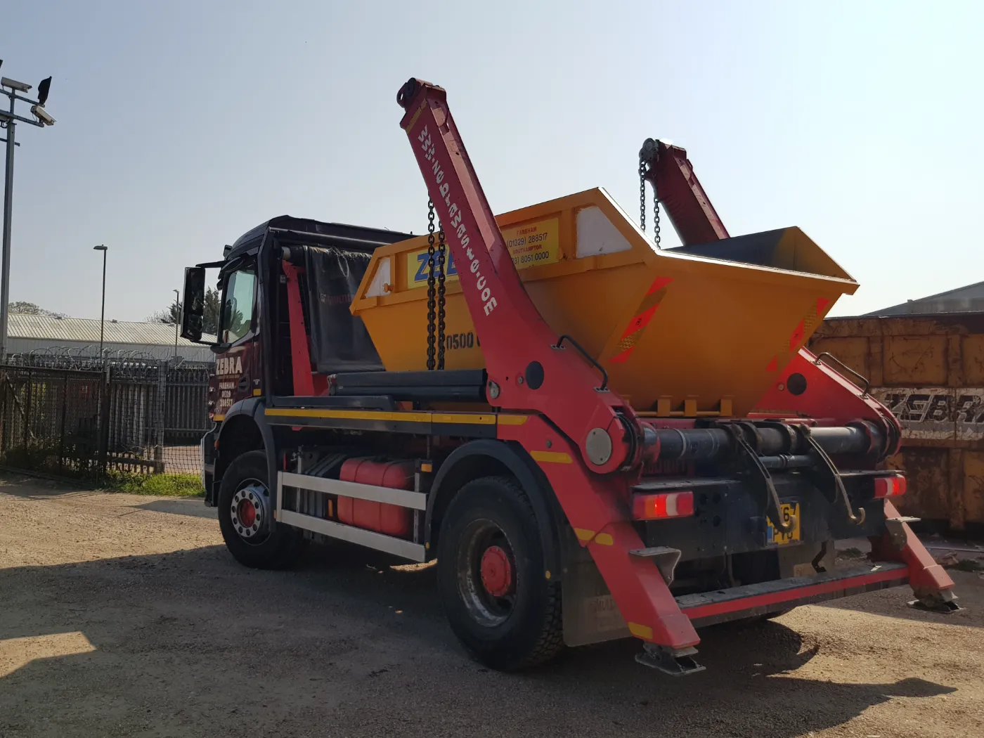 A Zebra skip loader carrying a yellow skip