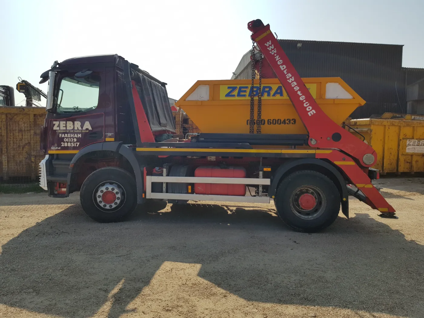 A Zebra skip lorry carrying a yellow skip